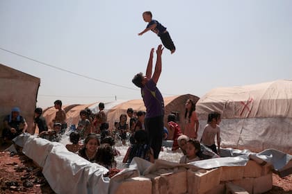 Un grupo de niños es supervisado por algunos adultos en una piscina improvisada en medio de las altas temperaturas en un campamento para desplazados internos en Zardana, en la provincia de Idlib, en el noroeste de Siria