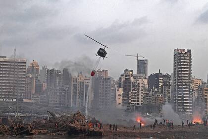 Un helicóptero intenta apagar varios incendios en la escena de la explosión masiva que golpeó el puerto de Beirut el 4 de agosto de 2020