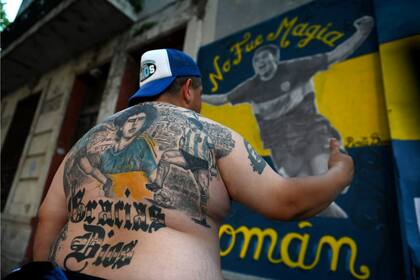 Un hincha, con Maradona en su espalda, observa un mural de Riquelme