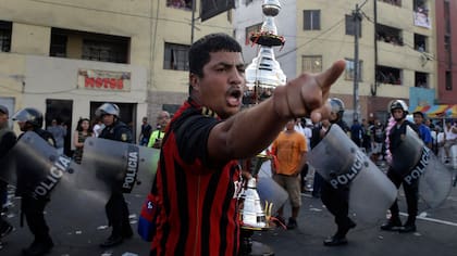 Un hincha del equipo de fútbol "Purito Barrios Altos" grita a los aficionados rivales que no están de acuerdo con la decisión del árbitro mientras corre con el trofeo de su equipo después de ganar el campeonato de fútbol callejero Mundialito de El Porvenir en Lima, Perú.