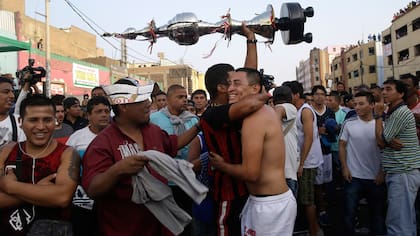 Un hincha del equipo de fútbol "Purito Barrios Altos" sostiene el trofeo en alto mientras se abraza a un jugador de su equipo después de ganar el campeonato de fútbol callejero Mundialito de El Porvenir en Lima, Perú.