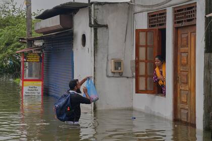 Un hombre brinda ayuda a una mujer atrapada en una casa en una zona inundada de Colombo, Sri Lanka