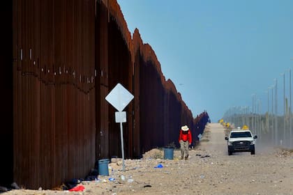 Un hombre camina a lo largo del muro fronterizo, al tiempo que un agente de la Patrulla Fronteriza de Estados Unidos patrulla el área, el martes 29 de agosto de 2023, cerca de Lukeville, Arizona (AP Foto/Matt York)