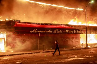 Un hombre camina frente a un incendio provocado durante las protestas en Minneapolis por la muerte de George Floyd en manos de la policía
