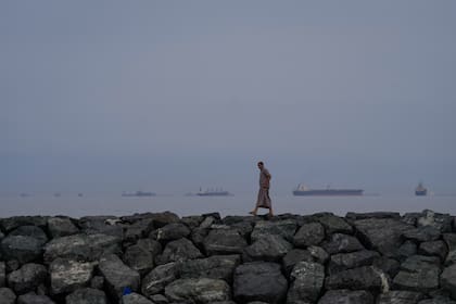 Un hombre camina por la orilla del mar mientras buques petroleros y de carga se alinean en el estrecho de Ormuz, vistos desde Khor Fakkan, Emiratos Árabes Unidos (AP Foto/Altaf Qadri/Archivo)
