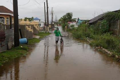 Un hombre camina por una calle inundada antes de la llegada del huracán Melissa, el lunes 27 de octubre de 2025, a Old Harbour, Jamaica. (AP Foto/Matías Delacroix)