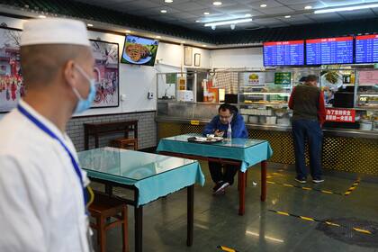 Un hombre come en un restaurante que solo tiene un asiento por mesa y marcas en el piso para imponer el distanciamiento social como medida preventiva contra la propagación del coronavirus, en Pekín el 17 de abril de 2020