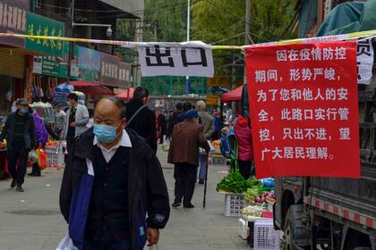 Un hombre con barbijo camina al lado de un aviso que anuncia las políticas de tránsito en las calles en Lanzhou