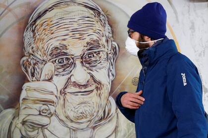 Un hombre con barbijo camina al lado de un mural del Papa Francisco en el metro de Roma