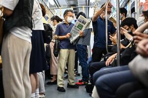 Un hombre con barbijo lee un periódico mientras viaja en un tren en Tokio el 15 de septiembre de 2020