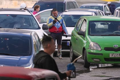 Un hombre con una chaqueta con los colores de la bandera de Venezuela hace fila para comprar combustible en una estación de servicio