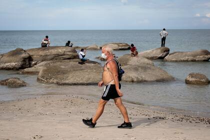 Un hombre con una máscara facial, en medio de la preocupación por la propagación del coronavirus, camina por la playa de Hua Hin en Tailandia el 19 de mayo de 2020