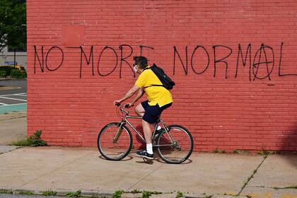 Un hombre con una máscara protectora monta una bicicleta junto a un graffiti que dice NO MÁS NORMAL durante la pandemia de coronavirus el 25 de mayo de 2020 en el distrito de Queens de la ciudad de Nueva York