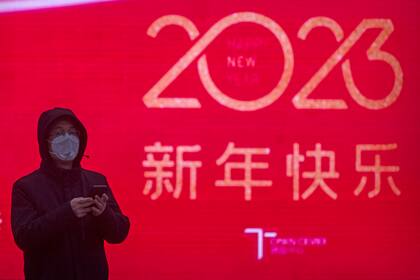 Un hombre con una mascarilla pasa frente a una gran pantalla que muestra un gráfico que celebra el próximo Año Nuevo Lunar en Pekín