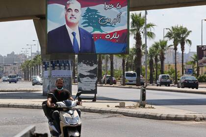 Un hombre conduce una moto frente a un cartel con una imagen del exprimer ministro libanés asesinado Rafiq al-Hariri, en una calle de su ciudad natal, en el sur de Sidón, la tercera ciudad del Líbano
