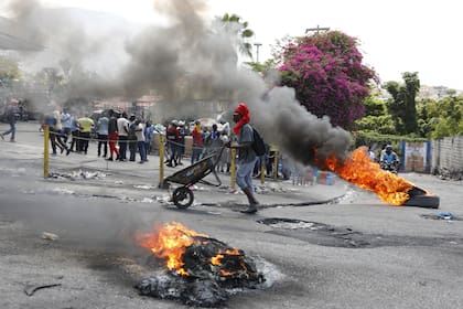 Un hombre empuja una carretilla frente a neumáticos en llamas durante una protesta para exigir la renuncia del primer ministro Ariel Henry, el jueves 7 de marzo de 2024, en Puerto Príncipe, Haití. 