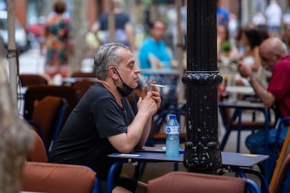 Un hombre fuma en un bar con terraza en Barcelona, España, el viernes 14 de agosto de 2020. El ministro de Salud español, Salvador Illa, ha anunciado una serie de nuevas restricciones a nivel nacional para ayudar a combatir un aumento en los casos de COVID-19