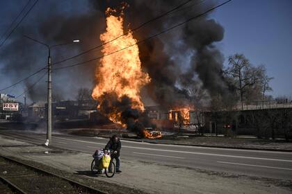 Un hombre huye con sus pertenencias mientras el fuego envuelve un vehículo y un edificio tras los disparos de artillería en la ciudad nororiental de Kharkiv el 25 de marzo de 2022.
