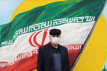 Un hombre iraní con un barbijo posa frente a una pintura mural de la bandera iraní en Teherán el 13 de abril de 2020 durante la pandemia del coronavirus