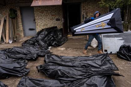 Un hombre lleva un ataúd junto a bolsas de plástico con cadáveres de civiles mientras la policía realiza investigaciones en Bucha, antes de enviar los cadáveres a la morgue.