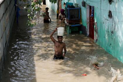 Un hombre lleva un balde de agua mientras camina por un carril inundado a orillas del río Yamuna en Delhi, India, 21 de agosto de 2019