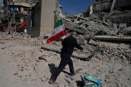 Un hombre lleva una bandera iraní para colocarla sobre los escombros de una instalación policial alcanzada durante la campaña militar en Teherán, Irán, el 4 de marzo de 2026