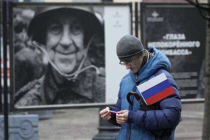 Un hombre lleva una bandera rusa junto a una exhibición de fotografías del Ministerio de Defensa de Rusia que muestra a participantes en eventos en Ucrania, durante la celebración del Día de la Unidad Nacional en San Petersburgo, Rusia, el sábado 4 de noviembre de 2023. 