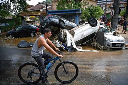 Un hombre pasa con su bicicleta por delante de los coches destruidos por una inundación repentina en Petrópolis, Brasil, el 16 de febrero de 2022. 