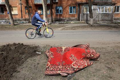 Un hombre pasa con su bicicleta por delante de un cuerpo cubierto por una alfombra tras los combates en las afueras de Mariupol, Ucrania, en el territorio bajo control del gobierno separatista de la República Popular de Donetsk, el martes 29 de marzo de 2022.