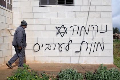 Un hombre pasa frente a una pared con un graffiti que dice en hebreo "venganza, muerte a los árabes", supuestamente pintado por colonos judíos en la aldea palestina de Turmus Ayya, en Cisjordania 