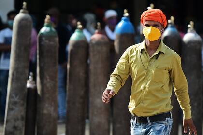 Un hombre pasa junto a personas que esperan para rellenar sus cilindros de oxígeno médico para pacientes con coronavirus en una estación de recarga de oxígeno en Allahabad, la India, el 24 de abril de 2021