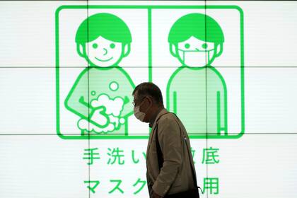 Un hombre pasa junto a un cartel de concienciación sobre el uso de mascarillas y lavado de manos para ayudar a frenar los contagios de coronavirus, el miércoles de 29 septiembre de 2021, en Tokio.