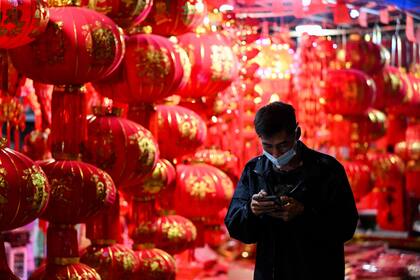 Un hombre que usa su teléfono móvil pasa frente a linternas chinas y otras decoraciones a la venta para las próximas celebraciones del Año Nuevo Lunar chino