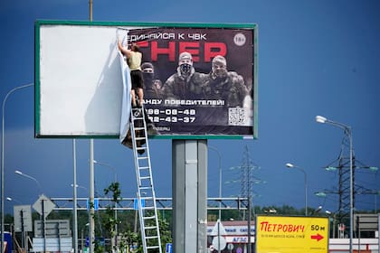 Un hombre retira el cartel con la leyenda "Únete a nosotros en Wagner", que se asocia con el propietario del contratista militar privado Wagner, Yevgeny Prigozhin, se ve por encima de una carretera en las afueras de San Petersburgo, Rusia, sábado, 24 de junio de 2023.