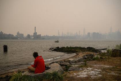 Un hombre se sienta ante el horizonte de la ciudad de Nueva York y el East River envueltos en humo en Brooklyn 