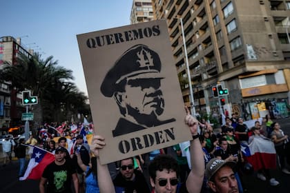 Un hombre sostiene un cartel que representa al general Augusto Pinochet, que gobernó Chile como dictador desde 1973 hasta 1990, con un texto que dice en español "Queremos orden", durante una protesta convocada tras el asesinato del agente de policía Daniel Palma, en la plaza Baquedano de Santiago de Chile, jueves 6 de abril de 2023. 