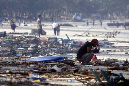 Un hombre tailandés rodeado por el daño causado por un tsunami se agacha en la arena de la playa de Patong en Phuket, el 27 de diciembre de 2004.