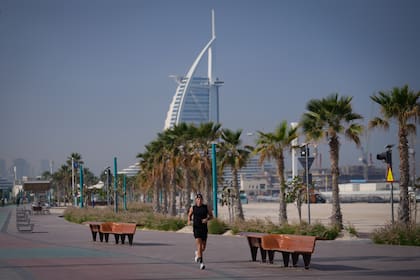 Un hombre trota por una playa con el hotel de lujo Burj Al Arab al fondo, en Dubai