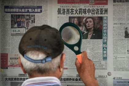 Un hombre utiliza una lupa para leer el titular de un periódico que informa sobre la visita a Asia de la presidenta de la Cámara de Representantes de Estados Unidos, Nancy Pelosi, en un puesto en Pekín, el domingo 31 de julio de 2022