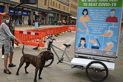 Un hombre y su perro pasan junto a una promoción financiada por el Consejo de Calderdale que aconseja a las personas sobre cómo frenar la propagación del coronavirus, en Halifax, en el norte de Inglaterra, el 9 de agosto de 2020