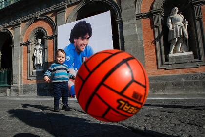 Un iño juega a la pelota frente a un mural de Maradona pintado en la fachada del Palacio Real de Nápoles en la céntrica Piazza Plebiscito