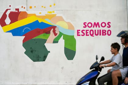 Un joven conduce una motocicleta frente a un mural con un mapa de Venezuela que incluye al territorio de Esequibo, una franja de tierra gestionada y controlada por Guyana, pero que Venezuela reclama como propia, el 11 de diciembre de 2023, en el vecindario 23 de Enero, en Caracas.