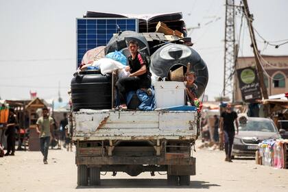 Un joven y una niña viajan en la parte trasera de un camión cargado con paneles solares, cisternas y otros artículos que pasan por las tiendas de campaña y refugios de personas desplazadas por el conflicto en la parte occidental de Rafah, en el sur de la Franja de Gaza, el 14 de junio de 2024