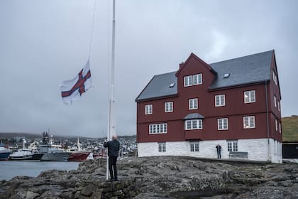 Un jubilado iza la bandera de las Islas Feroe frente a un edificio gubernamental en Tórshavn, bajo las fuertes ráfagas de viento