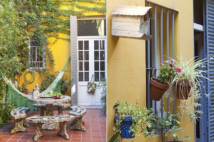 Un juego de bancos y mesa de azulejos partidos evoca el pasado e invita a disfrutar en el presente. Alrededor, la enorme enredadera se extiende casi por sobre el vidrio de la ventana y hasta la puerta, aportando un verde intenso