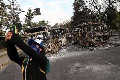 Un manifestante encapuchado se saca una foto con los colectivos incendiados