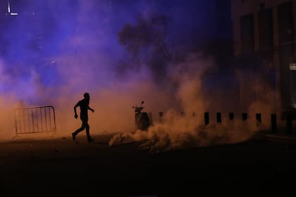 Un manifestante libanés corre a cubrirse mientras las fuerzas de seguridad arrojan gases lacrimógenos cerca de una calle de acceso al parlamento en el centro de Beirut el 9 de agosto de 2020