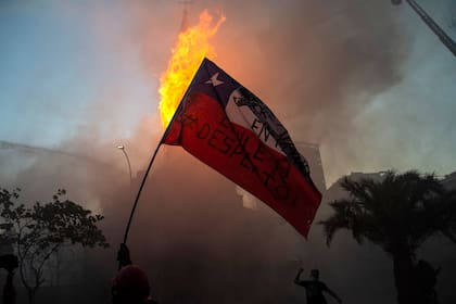 Un manifestante ondea una bandera chilena frente a la iglesia en llamas de Asunción, en la conmemoración del primer aniversario del levantamiento social en Chile