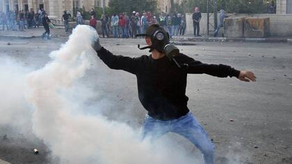 Un manifestante palestino le lanza de vuelta una granada con gas lacrimógeno a las fuerzas israelíes