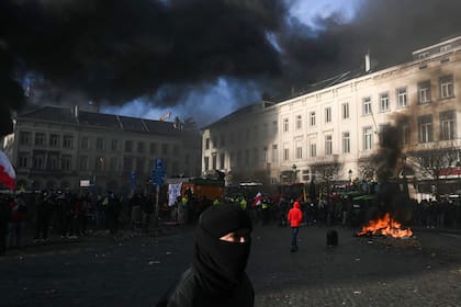 Un manifestante pasa junto a agricultores junto a tractores y una hoguera cerca del Parlamento Europeo en la Plaza de Luxemburgo, durante una protesta campesina para denunciar las reformas de la Política Agrícola Común (PAC) y acuerdos comerciales como el Mercosur, en Bruselas, el 18 de diciembre de 2025